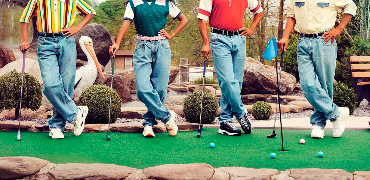 Four people wearing blue jeans and holding mini golf clubs on mini golf course